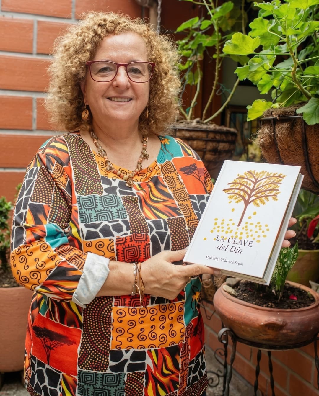 Clara Inés Valderrama Siegert sosteniendo su libro La Clave del Día en su jardín